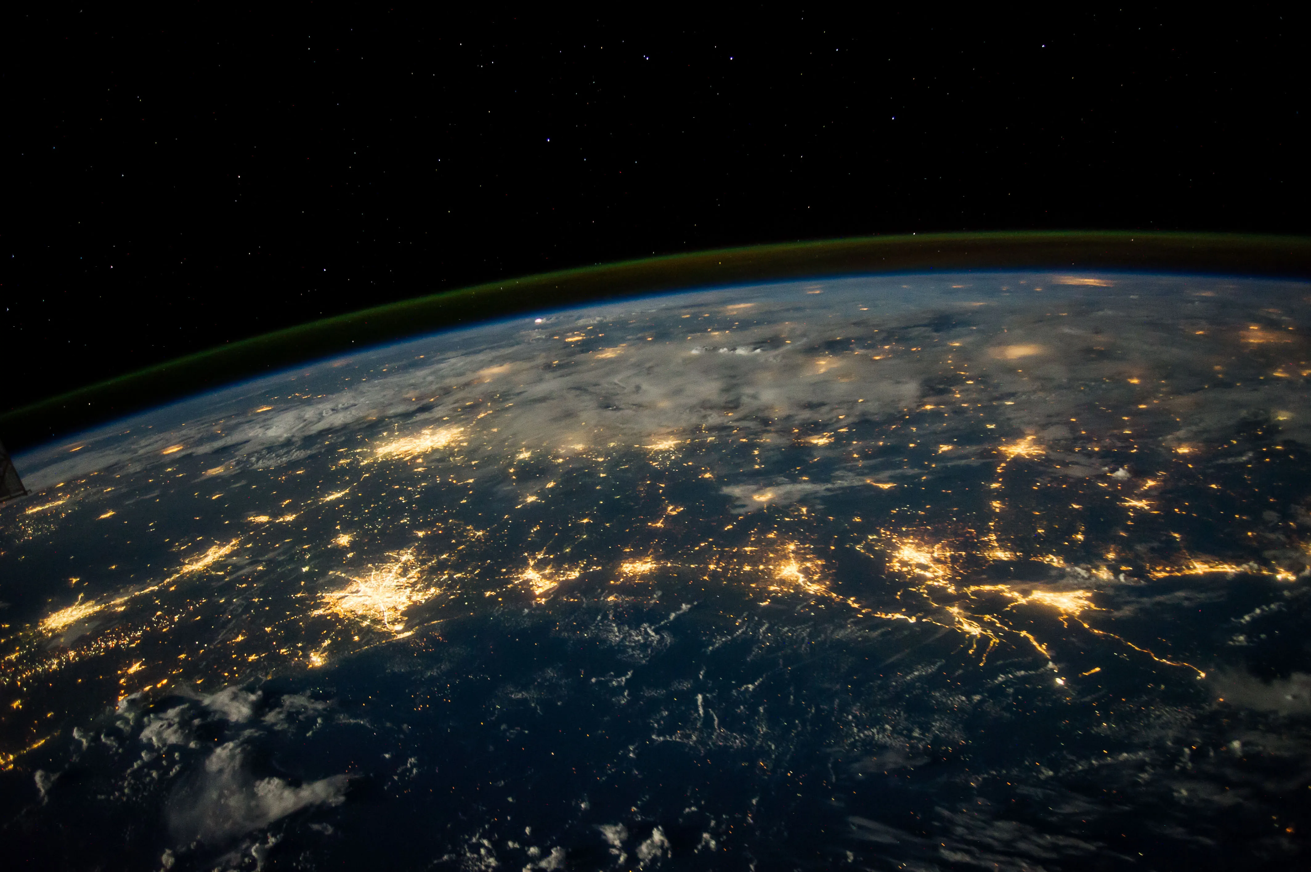 Earth at night from the International Space Station, with city lights below the blue atmospheric horizon